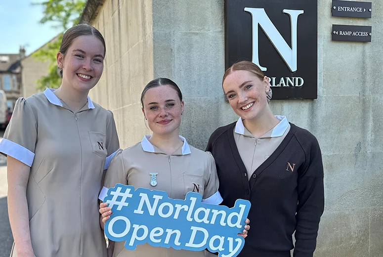 Three Norland students holding a sign that says Norland open day